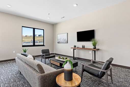 A living room with a grey couch, a black chair, a wooden coffee table, and a flat screen TV mounted on the wall.