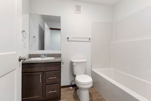 A white toilet sits in a bathroom next to a sink and a bathtub.