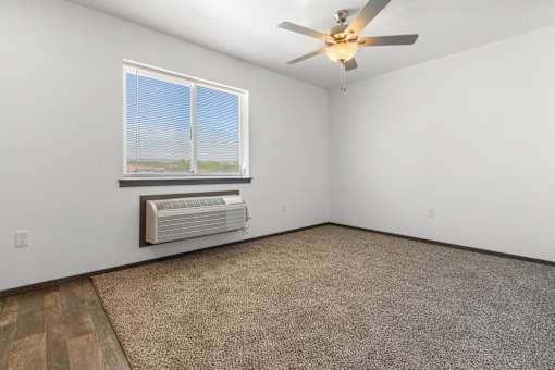 A room with a ceiling fan, carpeted floor, and a window with blinds.
