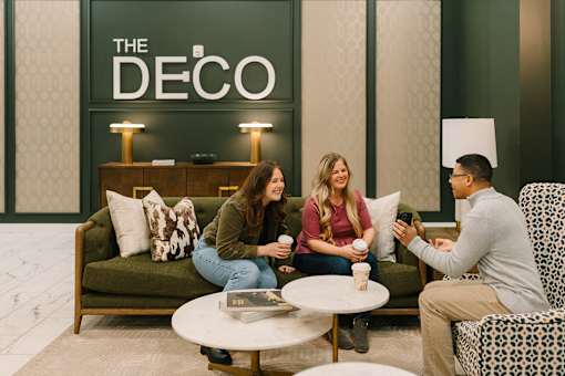 Three people are sitting on a green couch in a room with a sign that says "The Deco."
