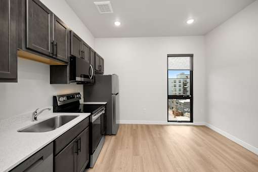 A kitchen with black cabinets and a window showing a building.