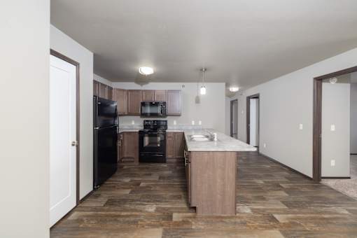 A kitchen with black appliances and a wooden floor.