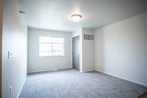 A spacious room with a window and carpeted floor.