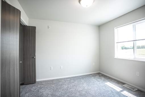 A room with a grey carpet and a window with a white frame.