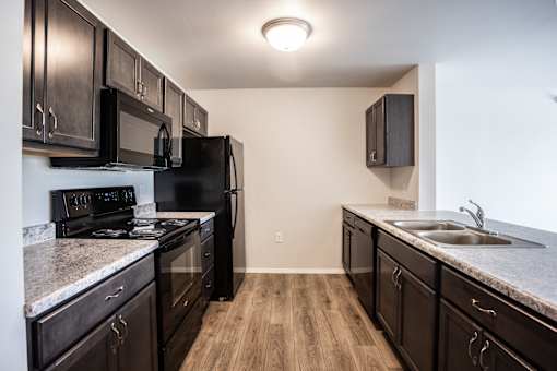 A kitchen with black appliances and wooden floors.