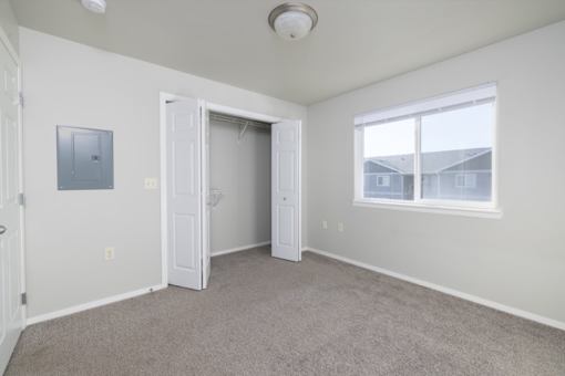 A room with a carpeted floor, a window, and a door leading to another room.