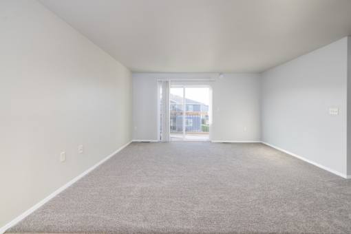 A large empty room with a carpeted floor and a doorway leading to another room.