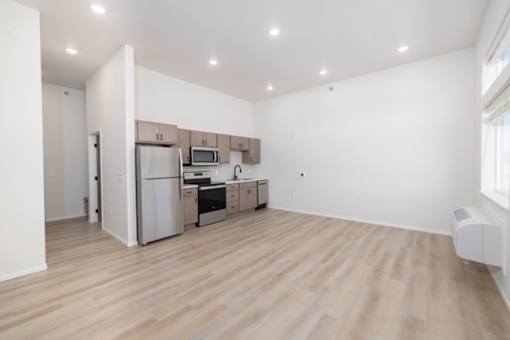 A kitchen with white walls and wooden floors with a refrigerator, microwave, oven, and sink.