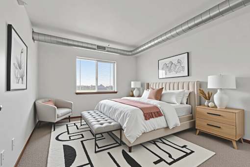 A bedroom with a large bed, a bench, and a rug with a black and white design.