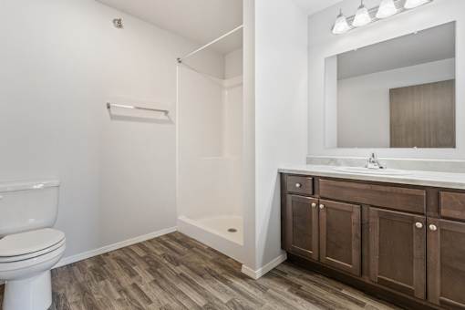 A white toilet sits in a bathroom with wood flooring and a white sink.