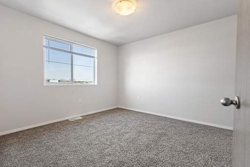 A room with a carpeted floor, a window, and a door.