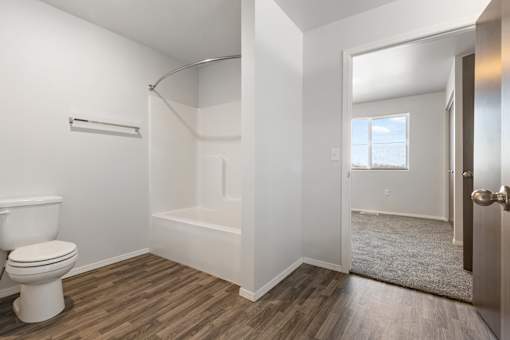 A white toilet sits next to a bathtub in a bathroom with wood flooring.