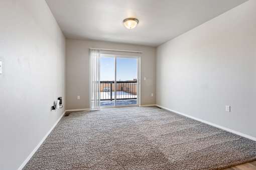 A room with a carpeted floor and a sliding glass door leading to a balcony.