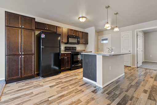 A kitchen with a black refrigerator and wooden cabinets.