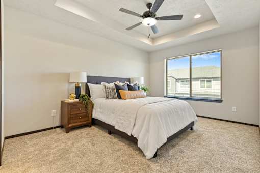 A bedroom with a large bed, a ceiling fan, and a window overlooking a building.