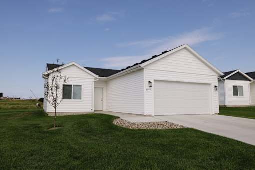 A white house with a garage door and a small tree in front.