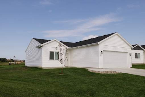A white house with a black roof and a small tree in front.