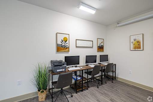 A room with a desk, chairs, and three framed pictures on the wall.