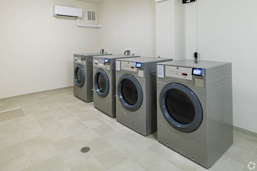 Three front loading washing machines are lined up in a laundry room.