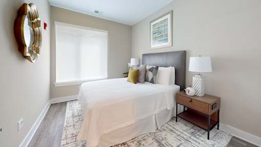 A bedroom with a large bed, a nightstand, and a mirror on the wall.