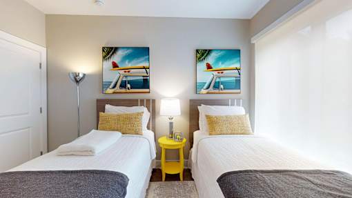 Two twin beds in a room with yellow side tables and beach-themed pictures on the wall.