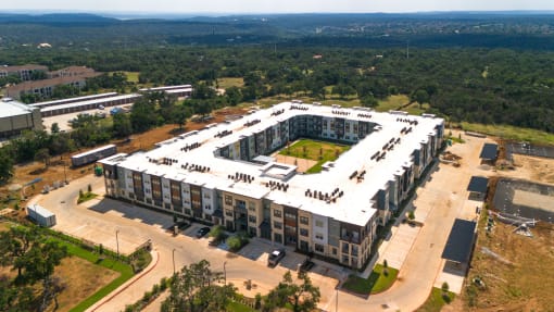 an aerial view of an apartment complex with a parking lot and trees at Birdie on Woodland Greens, Austin, TX