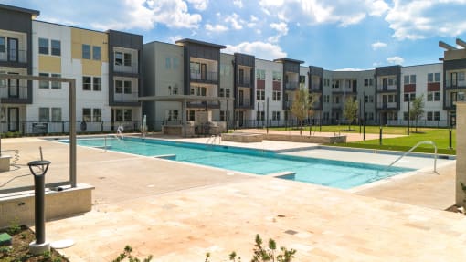 an outdoor pool with an apartment building in the background at Birdie on Woodland Greens, Texas