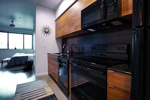 Contemporary kitchen with black appliances and wood finishes at THE'68 Apartments, San Antonio
