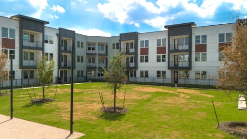 an exterior view of an apartment building with grass and trees at Birdie on Woodland Greens, Austin, TX