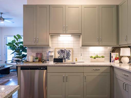 A kitchen with a stainless steel dishwasher and grey cabinets.