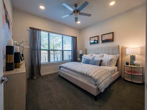 A bedroom with a large bed, a ceiling fan, and a window with curtains.