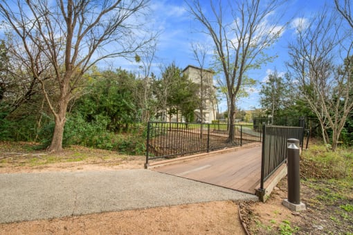 a bridge over a creek in a park with trees and a building in the background at Radius on Grove, Austin, TX