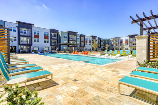 an outdoor pool with lounge chairs and a building with apartments in the background at Birdie on Woodland Greens, Texas