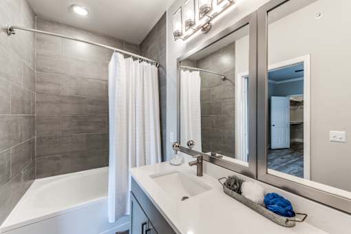 A modern bathroom with a white tub, sink, and grey tiled walls at Rosemary Apartments, Conroe, TX, 77384