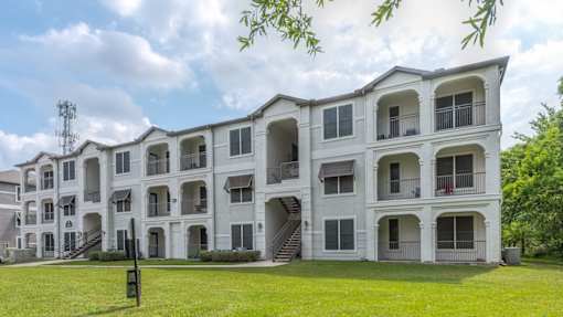 A large white apartment building with multiple balconies and a green lawn in front at Rosemary Apartments, Conroe, Texas