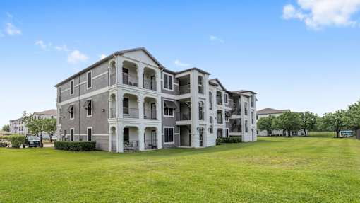 A large, grey apartment building with multiple balconies and doors at Rosemary Apartments, Conroe, TX