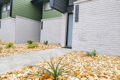 a sidewalk in front of a building with gravel and plants at Ivy Plains at Brooks Apartments, San Antonio