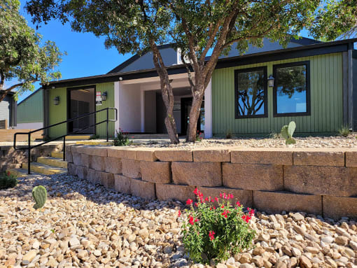 a house with a stone retaining wall and a tree in front of it at Ivy Plains at Brooks Apartments, Texas