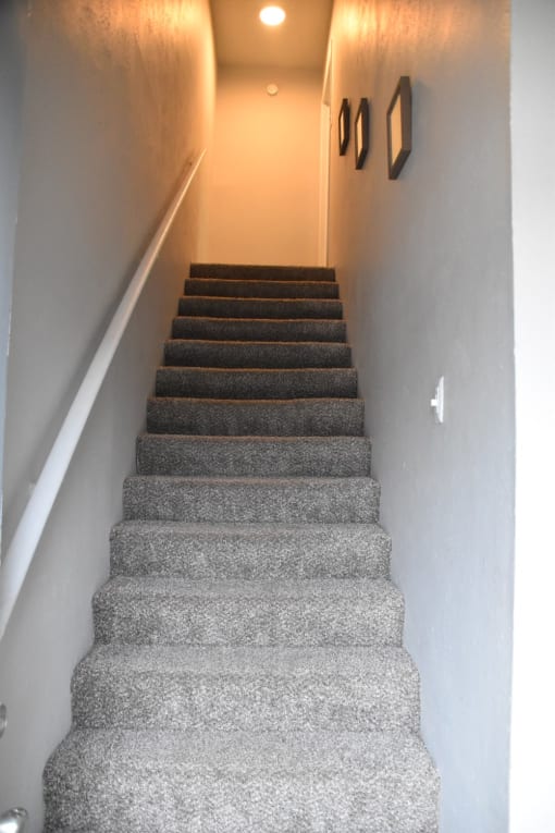 a flight of stairs leading up to a hallway with a white wall and a ceiling at Ivy Plains at Brooks Apartments, Texas