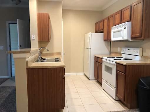 A kitchen with white appliances and wooden cabinets at Rosemary Apartments, Conroe, TX