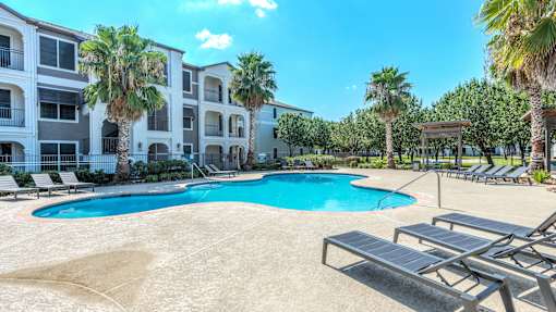 A swimming pool surrounded by sun loungers and palm trees in front of a multi-story apartment building at Rosemary Apartments, Conroe