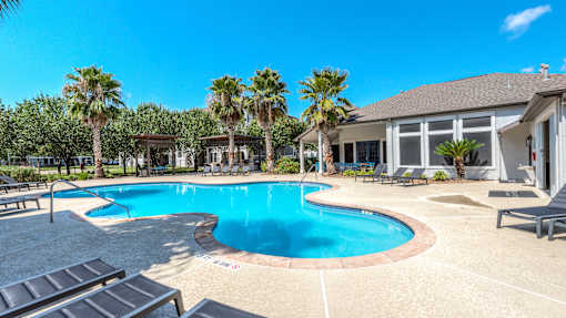 A swimming pool surrounded by palm trees and lounge chairs at Rosemary Apartments, Conroe, Texas