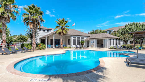 A large swimming pool surrounded by palm trees and lounge chairs at Rosemary Apartments, Conroe