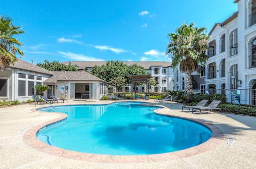 A large swimming pool in a residential area surrounded by palm trees at Rosemary Apartments, Conroe, TX
