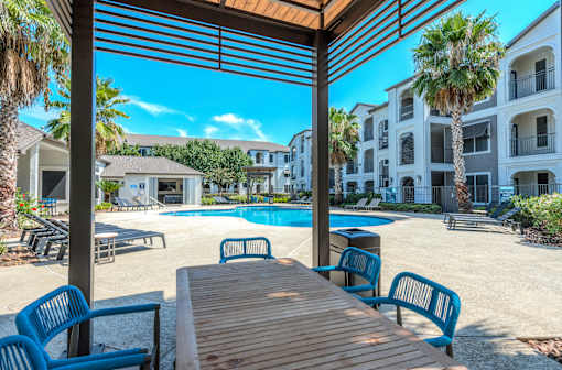 A wooden table is in the foreground of a sunny poolside area at Rosemary Apartments, Conroe, TX, 77384