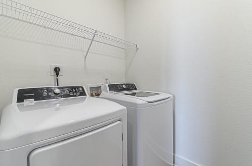 a white laundry room with two washes and a dryer at The Fitzroy San Marcos, San Marcos, TX