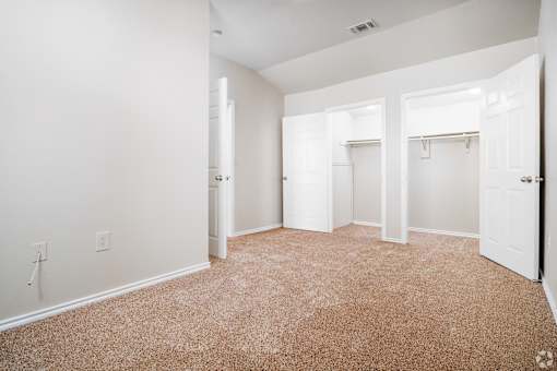 Empty bedroom with carpet and dual closets at Houston Street Townhomes Apartments, San Antonio