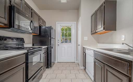 Galley kitchen with dark wood cabinets and black appliances at Houston Street Townhomes Apartments, Texas, 78220