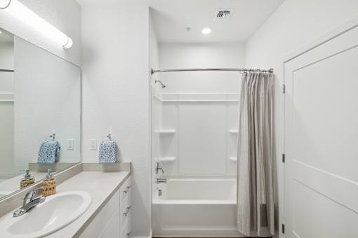 A white bathroom with a sink, mirror, and bathtub.