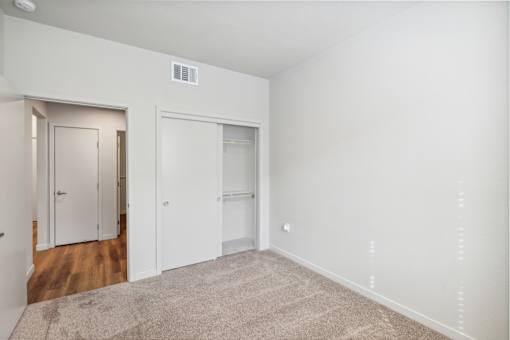 a bedroom with white walls and wood flooring and a closet